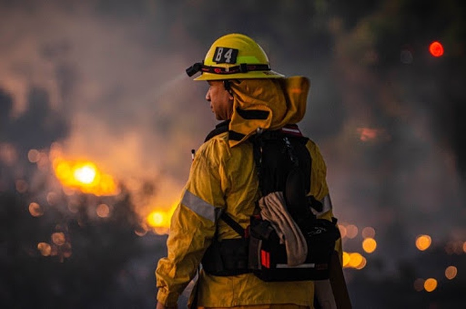 A person in uniform looks at a raging wildfire.