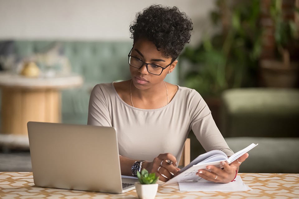 A women looking at her laptop while holding a notebook