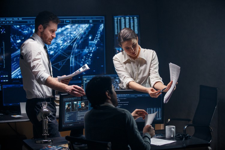 A team of counterterrorism analysts in a control room review a document.