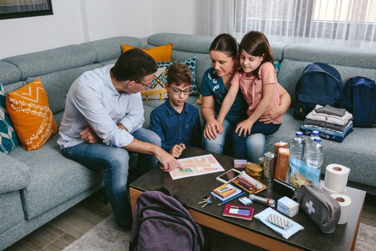A family of four discusses an emergency plan in their living room, with the contents of an emergency kit laid out on the coffee table.