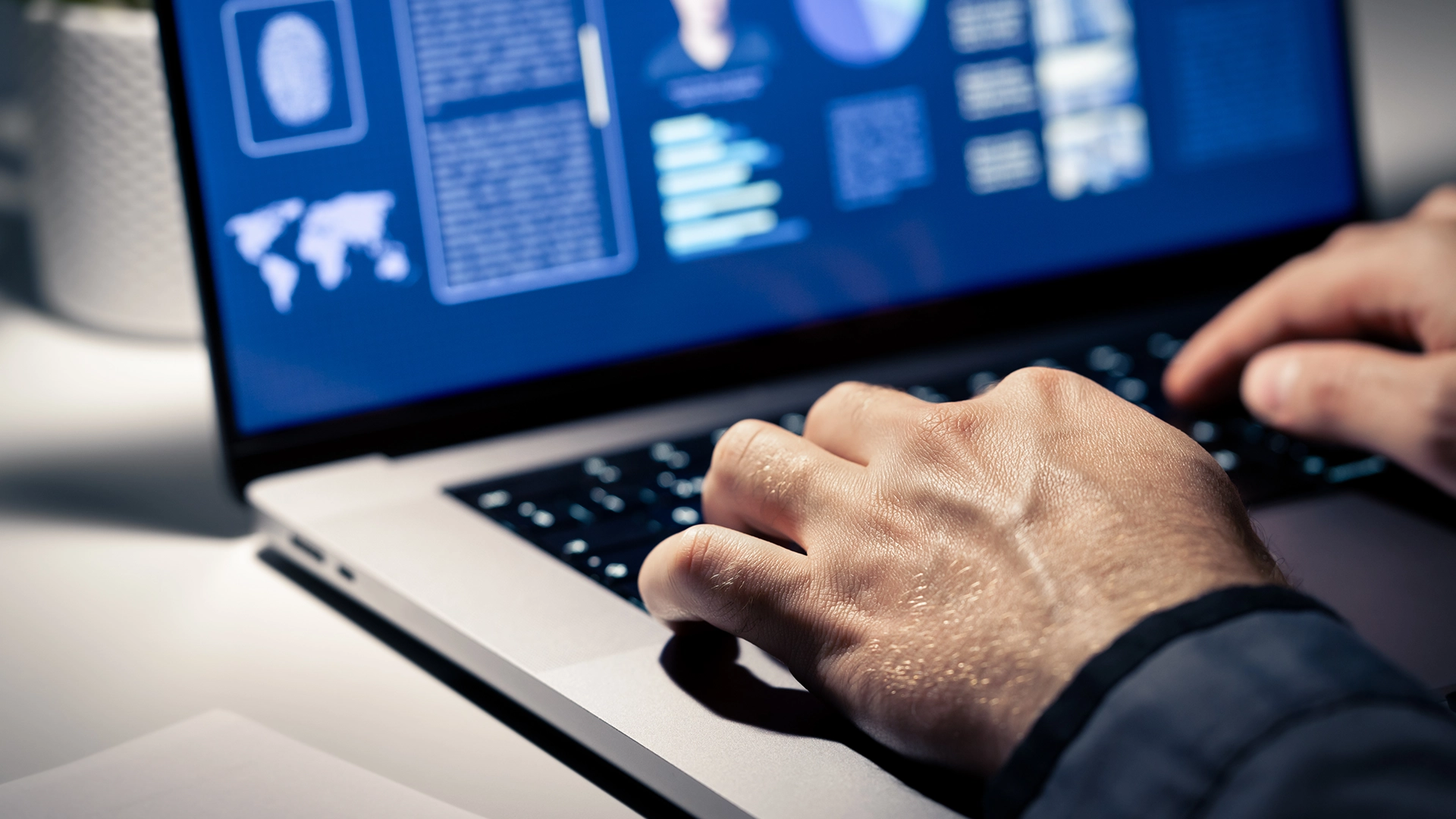 Hands typing on a laptop displaying digital graphics and charts.