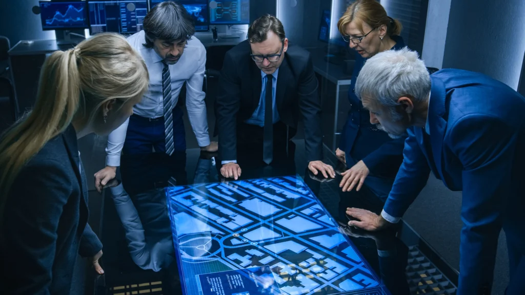 Professionals in suits examine a digital map on a table screen in a modern office.