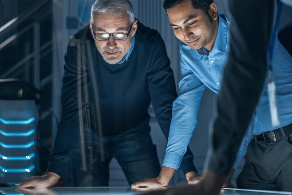 Two men in a high-tech environment study a large horizontal touch screen.
